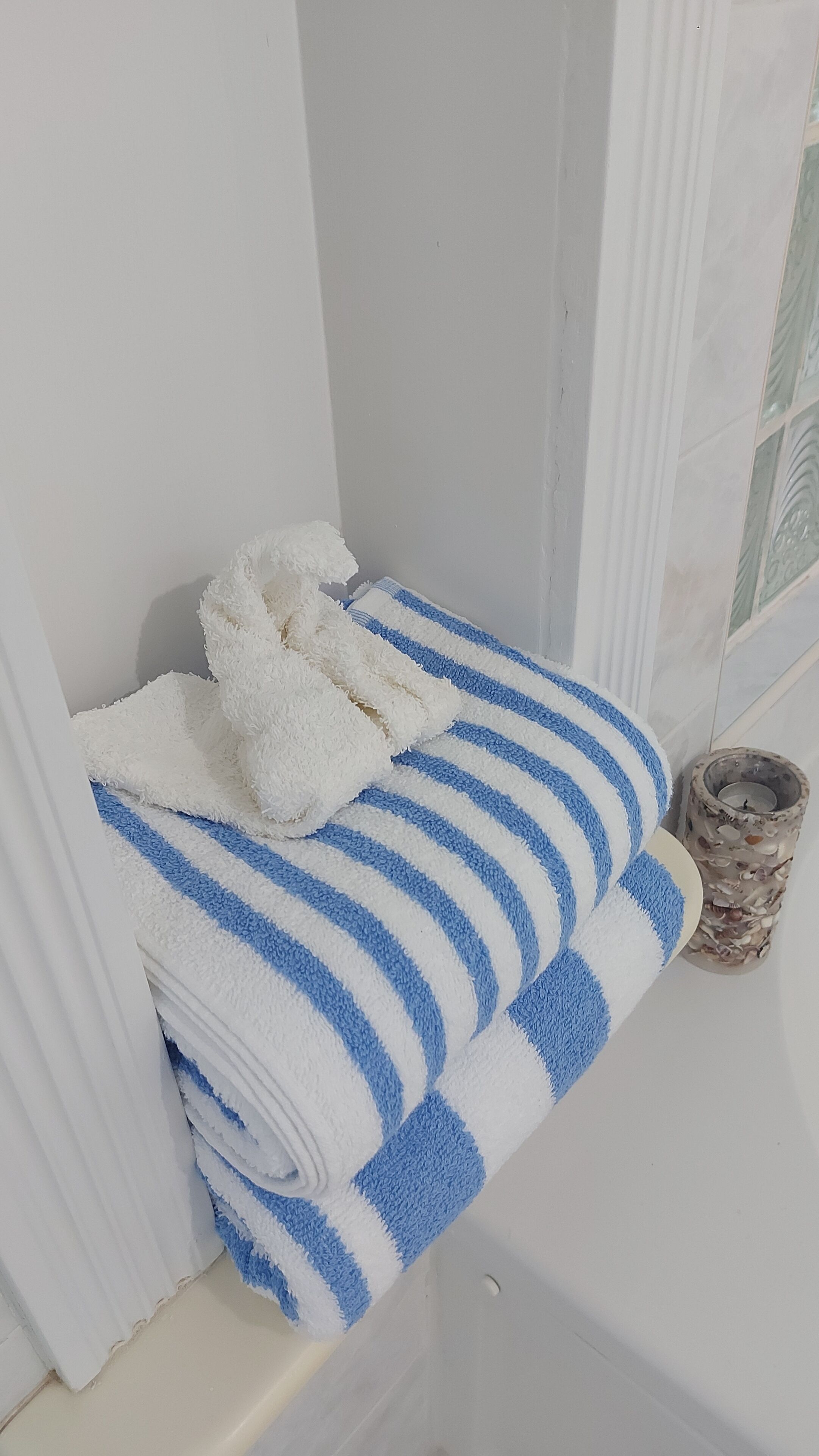 A bathroom with a white bathtub, a blue and white striped towel, and a decorative ceramic container.