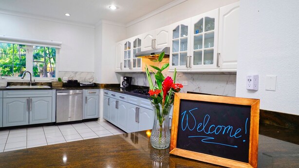 A kitchen with white cabinets, a marble countertop, and a welcome sign.