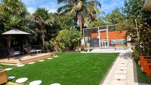 A backyard with artificial grass, a barbecue area, and a covered seating area.