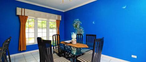A dining area with a glass table surrounded by chairs, a chandelier, and a window with curtains.