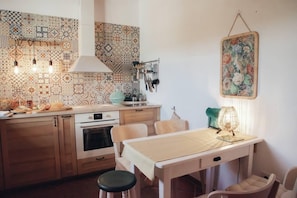 A kitchen with patterned tiles, wooden cabinets, a stove, and a dining area with a table and chairs. - Cosy Farmhouse Quinta da Eira 140 years old (Loule)