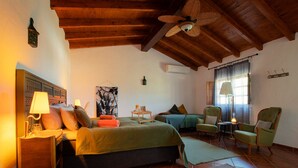 A cozy bedroom with a large bed, two chairs, a small table, and a ceiling fan.