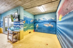 A room with a mural of ocean wildlife, a small table with decorative items, and a view of a house through a glass door.