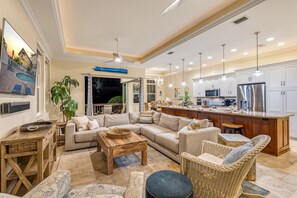 A spacious living room with a large sofa, a coffee table, and a dining area with wicker furniture.