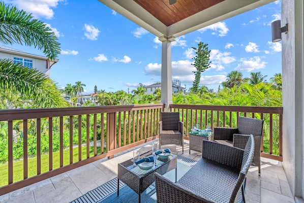 A covered outdoor seating area with wicker furniture and a view of a tropical landscape.