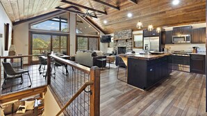 Amplio salón tipo loft con un gran ventanal, una chimenea de piedra y una cocina equipada con electrodomésticos modernos.