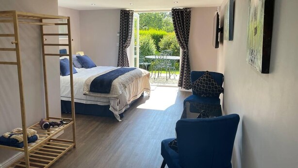 A bedroom with a bed, a chair, a wooden ladder, and a balcony with a view of greenery. - Brighouse Studio - Pet Friendly! - Free Parking (Brighouse)