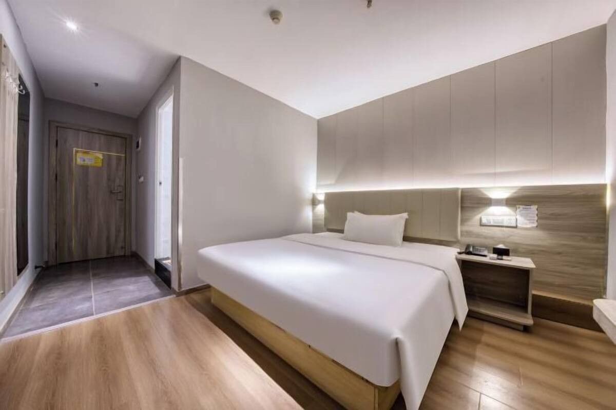 Une chambre d’hôtel moderne avec un grand lit, une table de chevet et une tête de lit en bois.