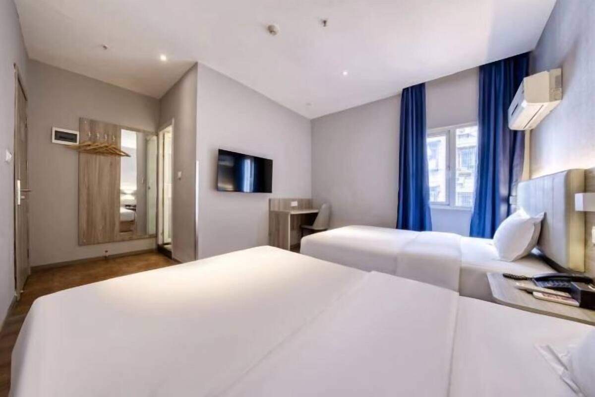 Une chambre d’hôtel moderne équipée de deux lits, d’une télévision, d’un bureau et d’une fenêtre avec des rideaux.