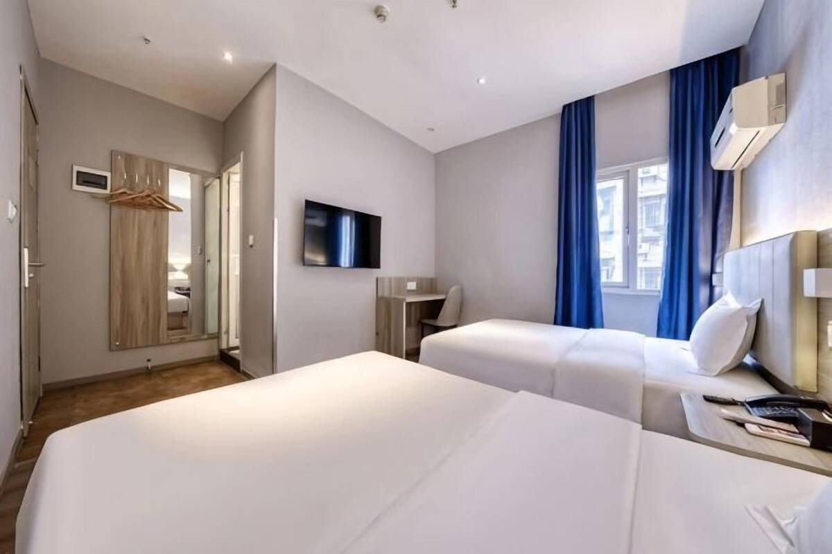 Une chambre d’hôtel avec deux lits, une télévision, une armoire et une fenêtre avec des rideaux.