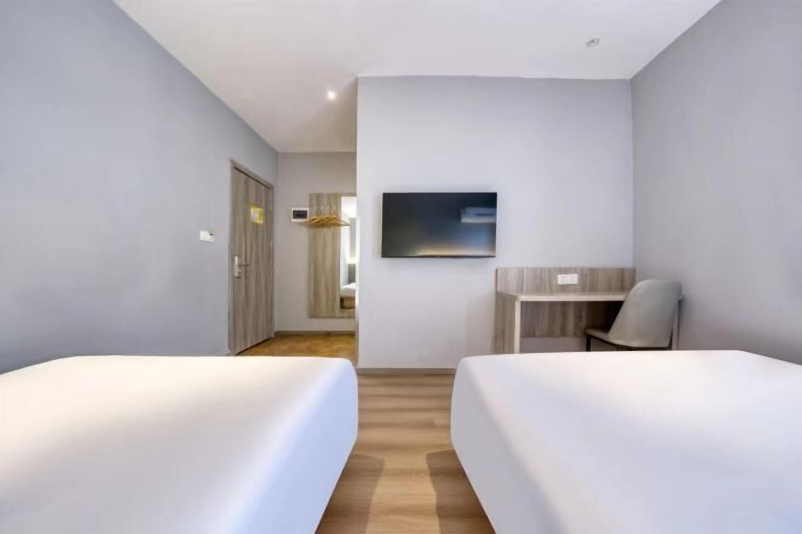 A hotel room with two beds, a desk, a chair, a TV, and a wardrobe.