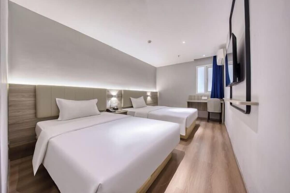 A hotel room with two beds, a desk, a chair, a TV, and a window with curtains.