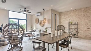 A modern dining area with a wooden table and chairs, a wicker chair, and a brick wall. - Stunning 3 bedroom condo near beach&downtown Tulum (Tulum)
