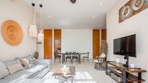 A modern living room with a sofa, a coffee table, a TV, and a dining area with chairs and a table. - Stunning 3 bedroom condo near beach&downtown Tulum (Tulum)
