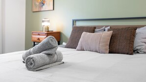 Una cama bien hecha con almohadas, una toalla doblada y una mesita de noche con una lámpara.