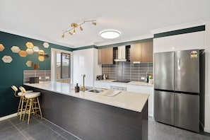 A modern kitchen with a central island, stainless steel appliances, and a unique hexagonal wall decoration. - Royal Romanesque holiday house in Dakabin / 3 min to shops (Dakabin)
