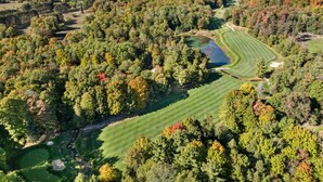 An aerial view of a golf course surrounded by dense forest with a lake in the background.