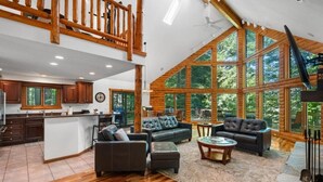 A spacious living area with a large window, a wooden ceiling, and a kitchen with dark cabinets.