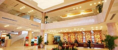 A hotel lobby with a reception desk, a staircase, and a chandelier.