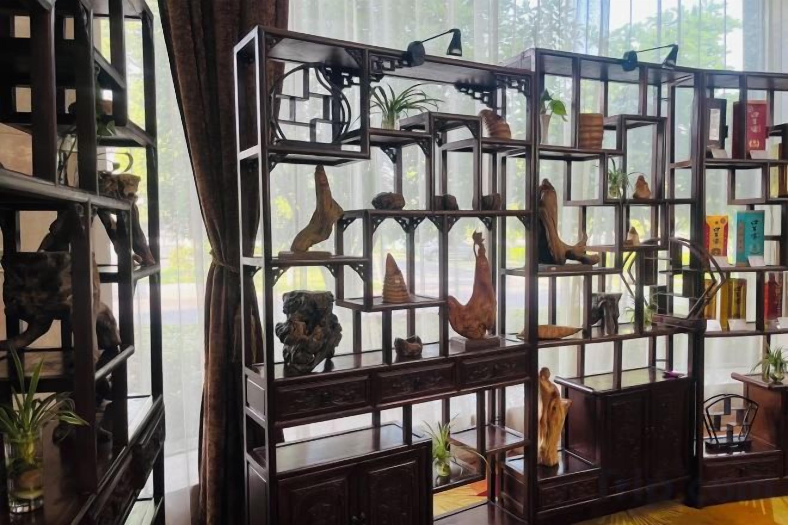 Una habitación con un ventanal grande, una estantería de madera con varios objetos decorativos, y una silla.