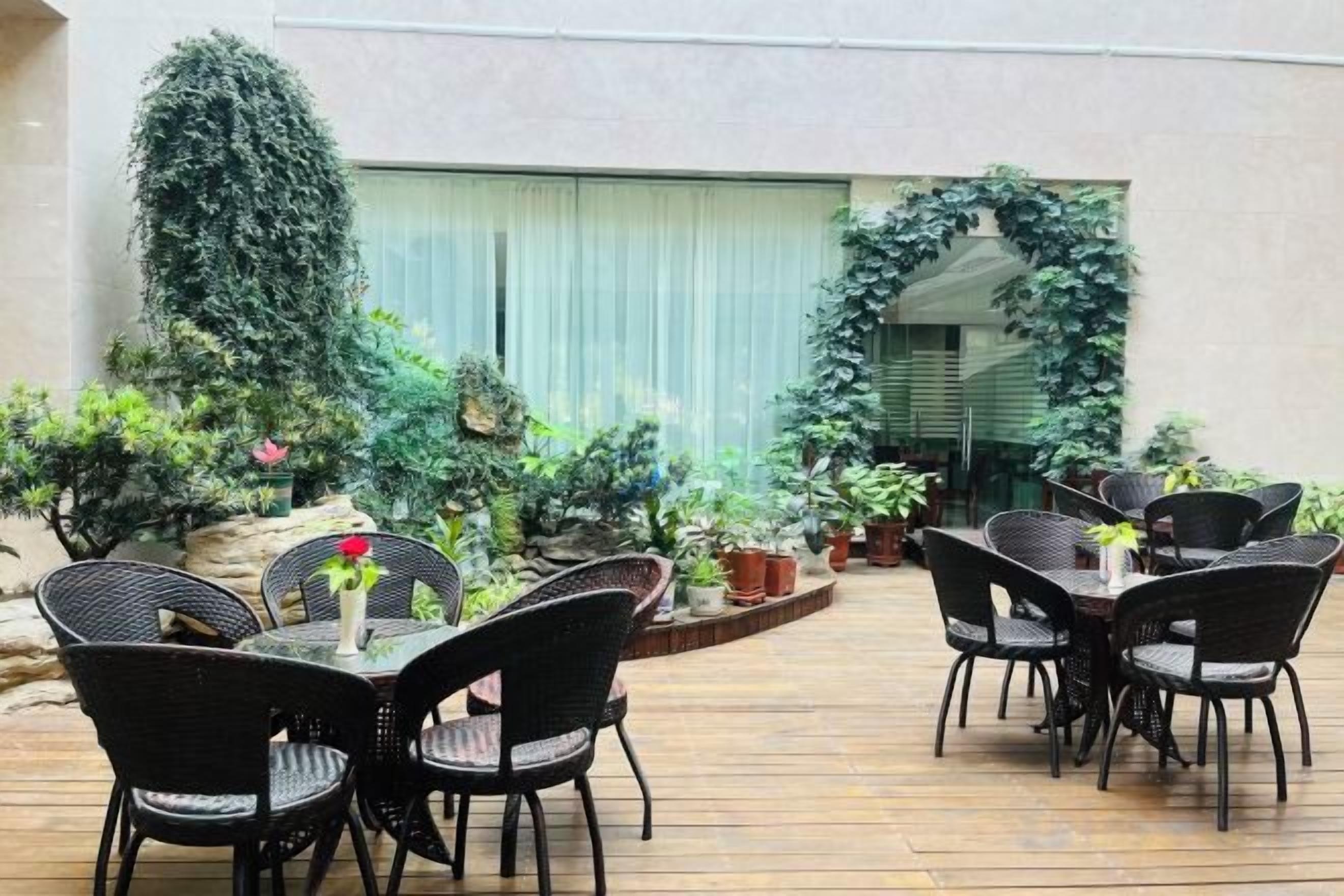 Un patio exterior con piso de madera, sillas de mimbre negro y una mesa con un jarrón de flores.