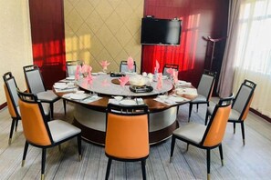 Una mesa redonda con ocho sillas, un televisor de pantalla plana montado en la pared y una cortina roja al fondo.