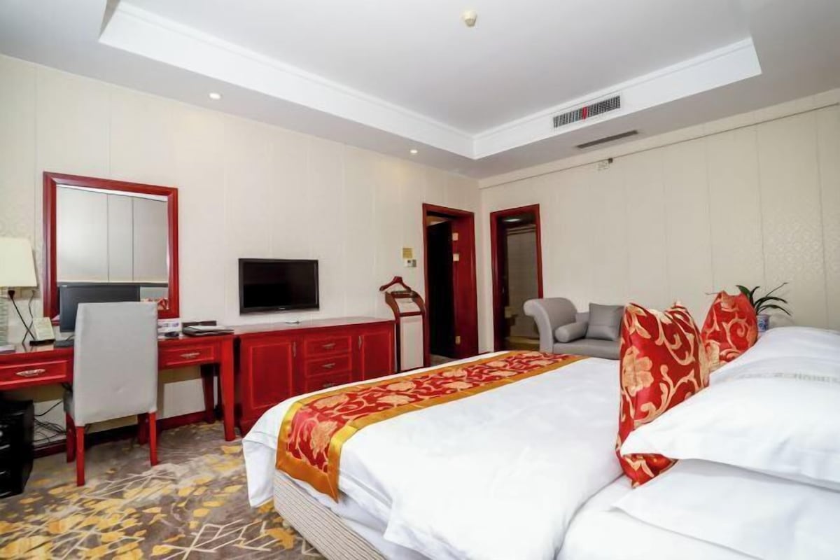 A hotel room with a bed, a desk with a computer, a television, and a chair.