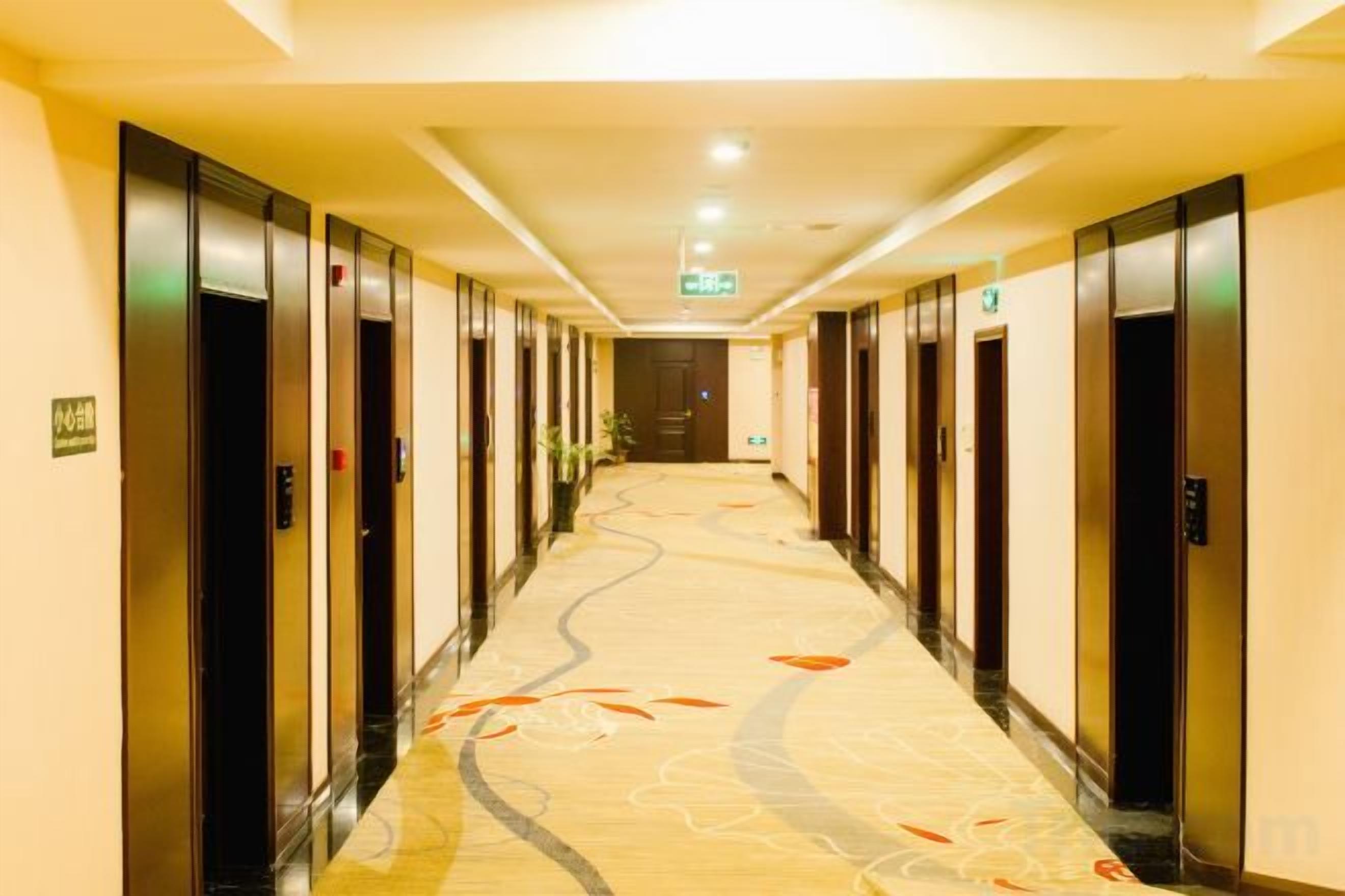 Un pasillo de hotel con piso alfombrado, puertas a ambos lados y una fuente de luz al final.