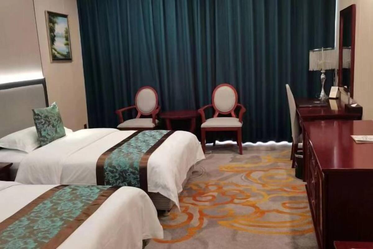 A hotel room with two beds, a desk, two chairs, and a large window with curtains.