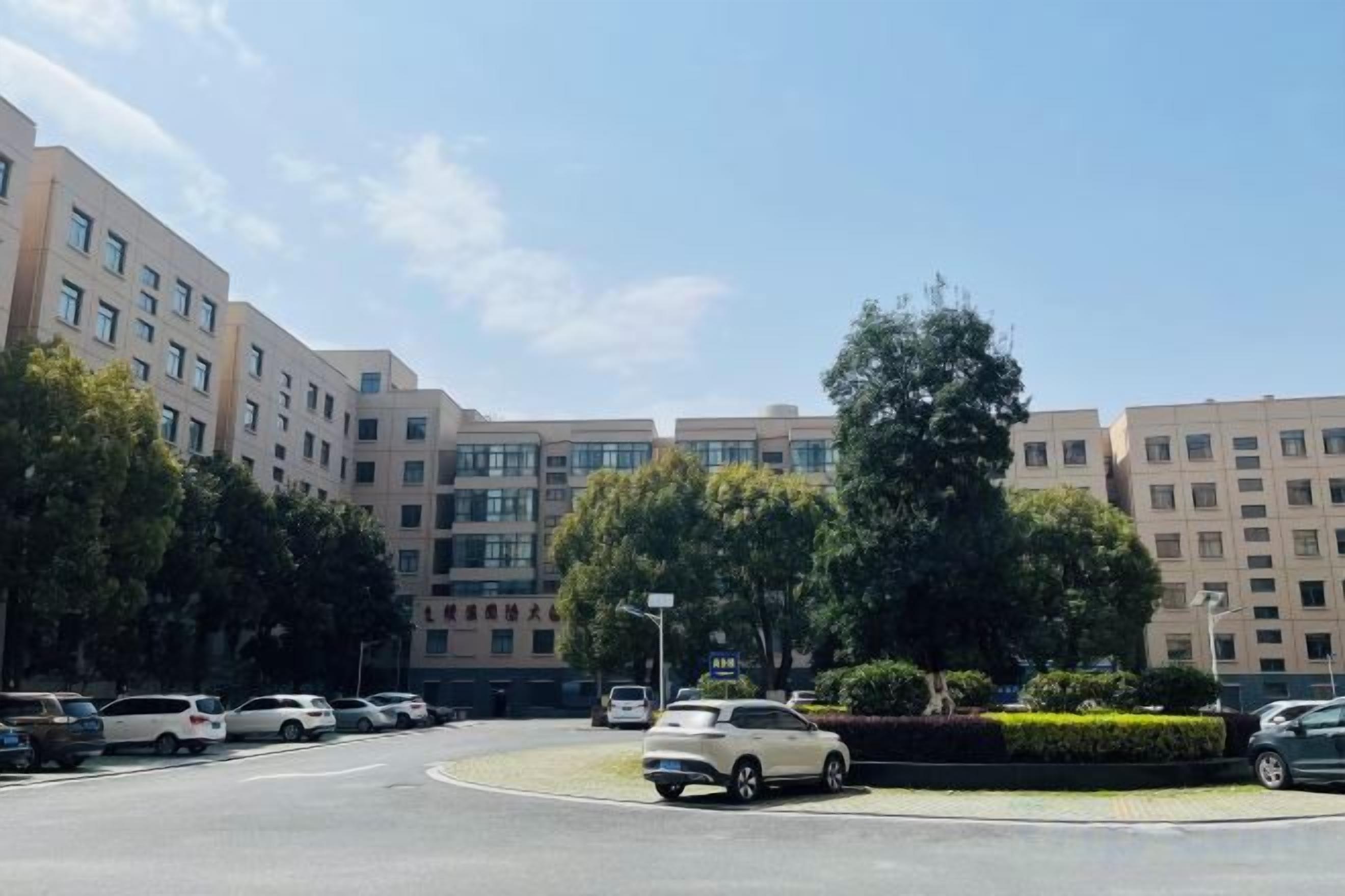 A parking lot with multiple cars, a roundabout, and a building with multiple floors and windows.