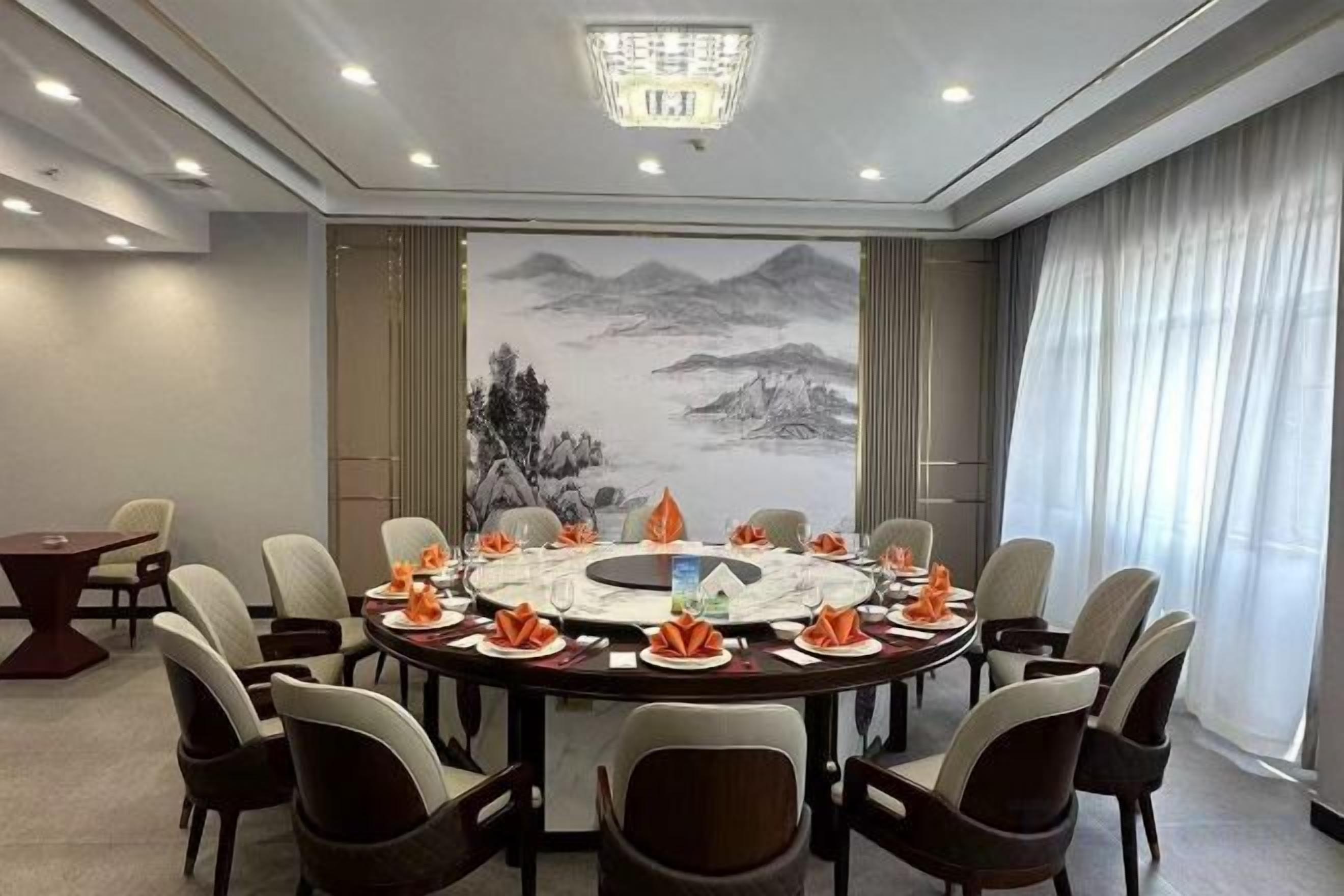 Un salón de conferencias con una mesa redonda, sillas y un cuadro grande de montañas.