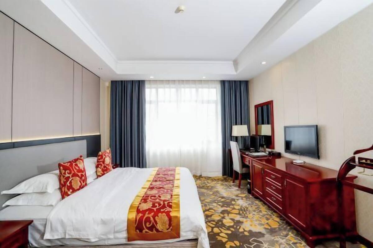 A hotel room with a bed, a desk, a TV, and a window with curtains.