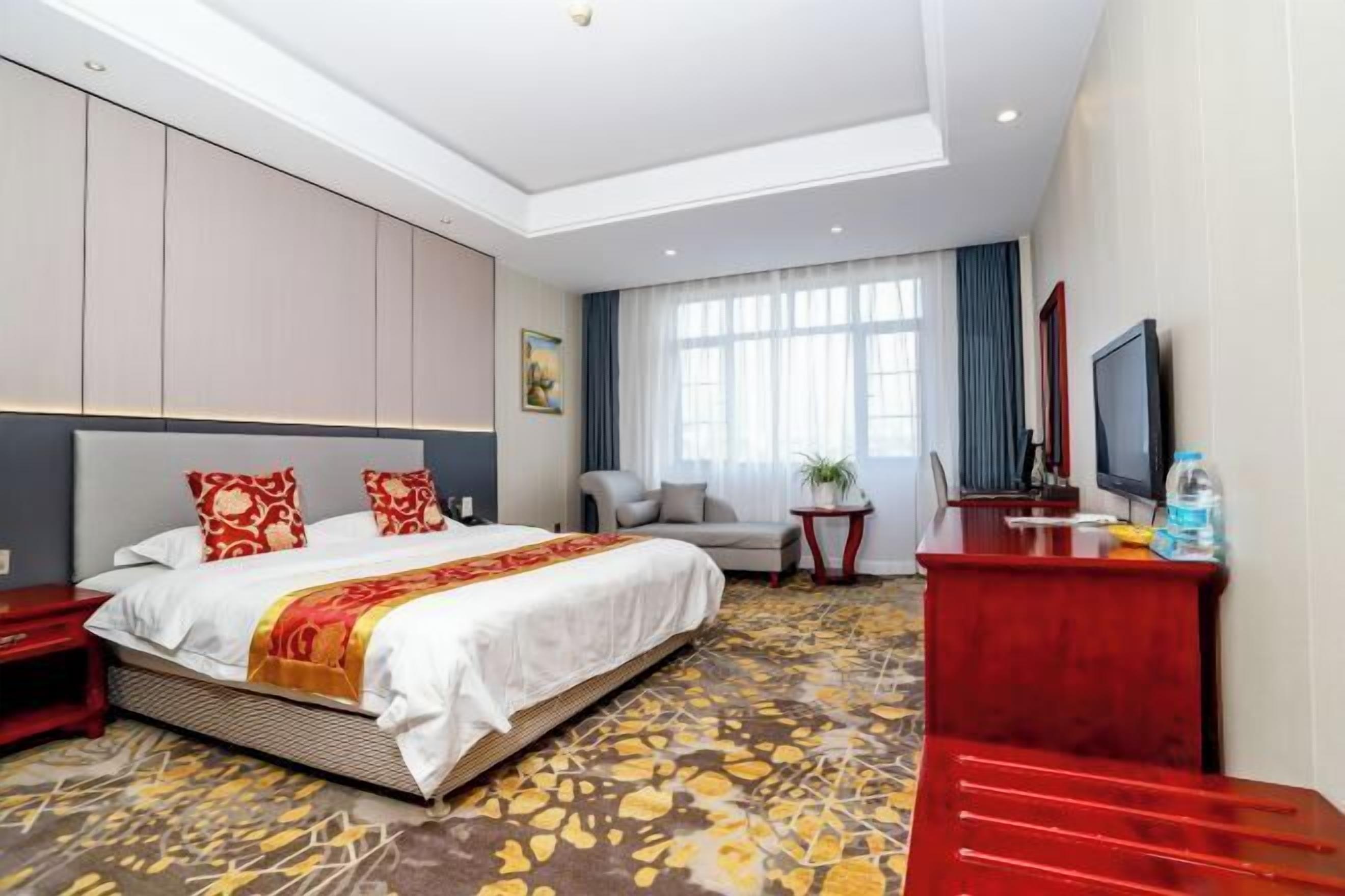 A hotel room with a bed, a desk, a TV, and a window with curtains.