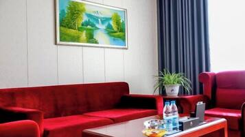 A red sofa, a small table with water bottles, a potted plant, and a painting of a landscape on the wall.
