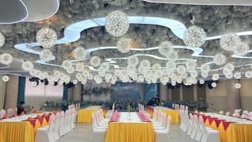 A banquet hall with multiple round tables, each with a white tablecloth and yellow runners.