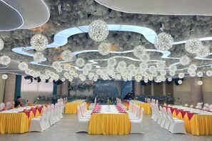 Un salón de banquetes con varias mesas redondas, cada una con mantel blanco y caminos de mesa amarillos.