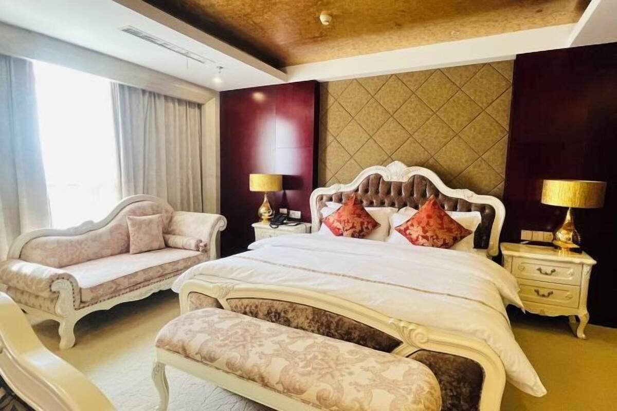A bedroom with a large bed, a sofa, a bench, and two bedside tables with lamps.