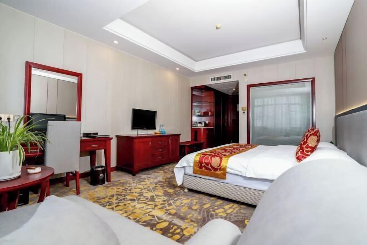 A hotel room with a bed, a desk, a television, a wardrobe, and a large mirror.