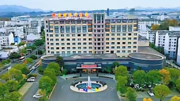 A multi-story hotel with a central courtyard, surrounded by trees and a parking area.