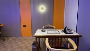A room with a table, chairs, a trash bin, and a wall-mounted light.