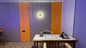 A room with a table, chairs, a trash bin, and a wall with a circular light fixture.