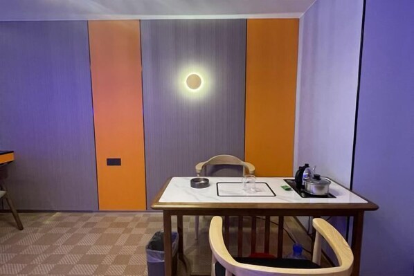 A room with a table, chairs, a trash bin, and a wall with a circular light fixture.