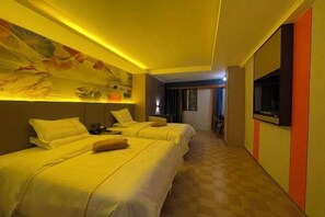 A hotel room with two beds, a mural on the wall, a television, and a check-in counter.