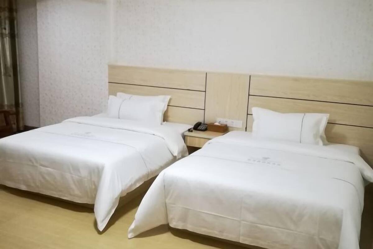 Twee enkele bedden met houten hoofdborden, witte beddengoed en een nachtkastje met een telefoon.