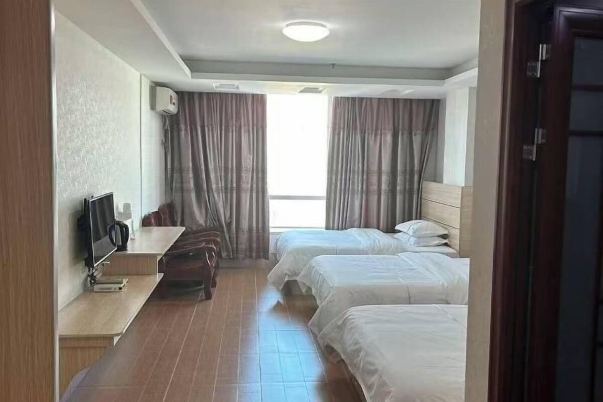 Hotelkamer met twee bedden, een bureau, een stoel, een televisie en een raam met gordijnen.