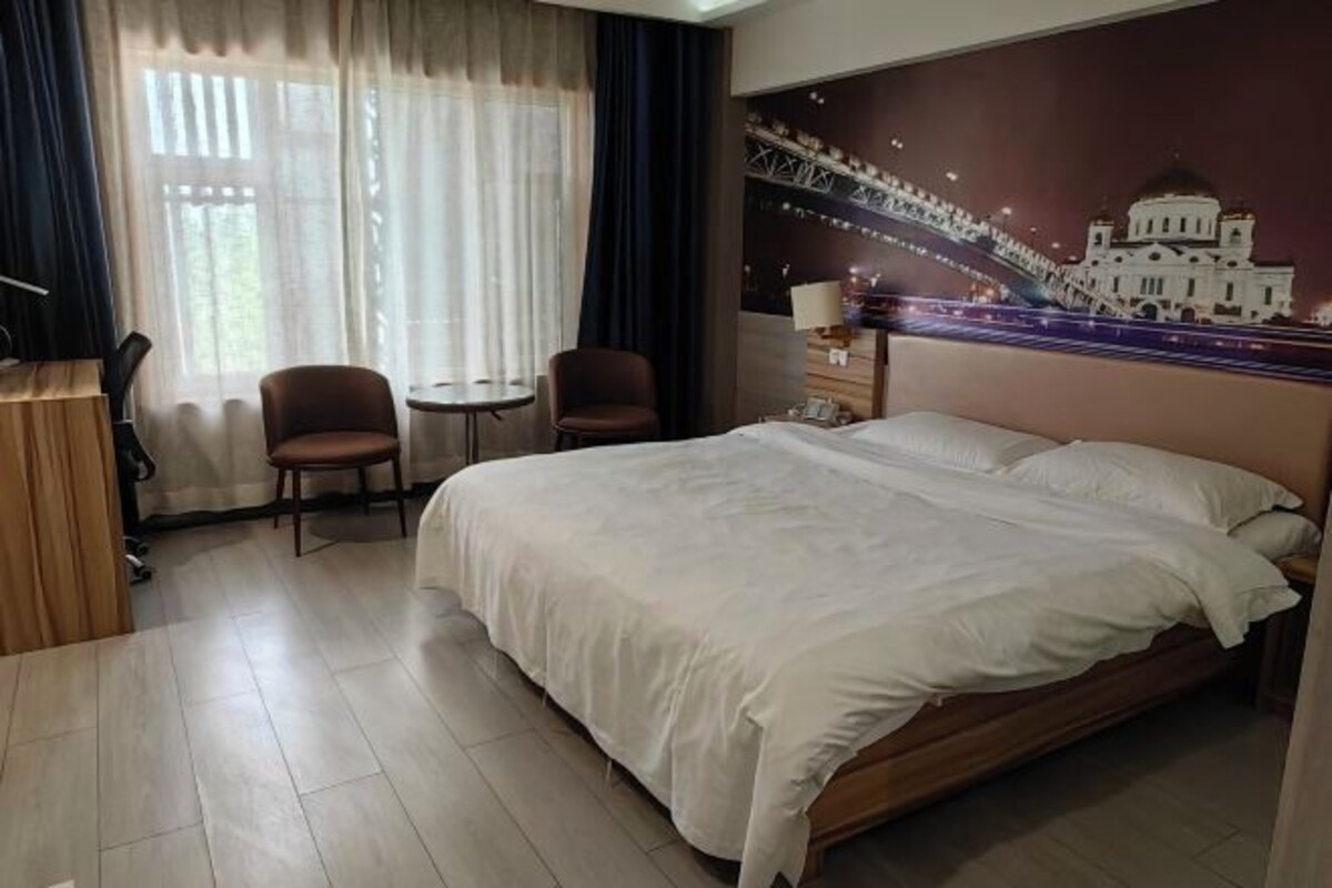 A hotel room with a large bed, two chairs, a small table, a desk, and a wall mural.