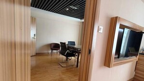 Una stanza con pavimento in legno, una scrivania con una sedia, una televisione a muro e una finestra con tende.