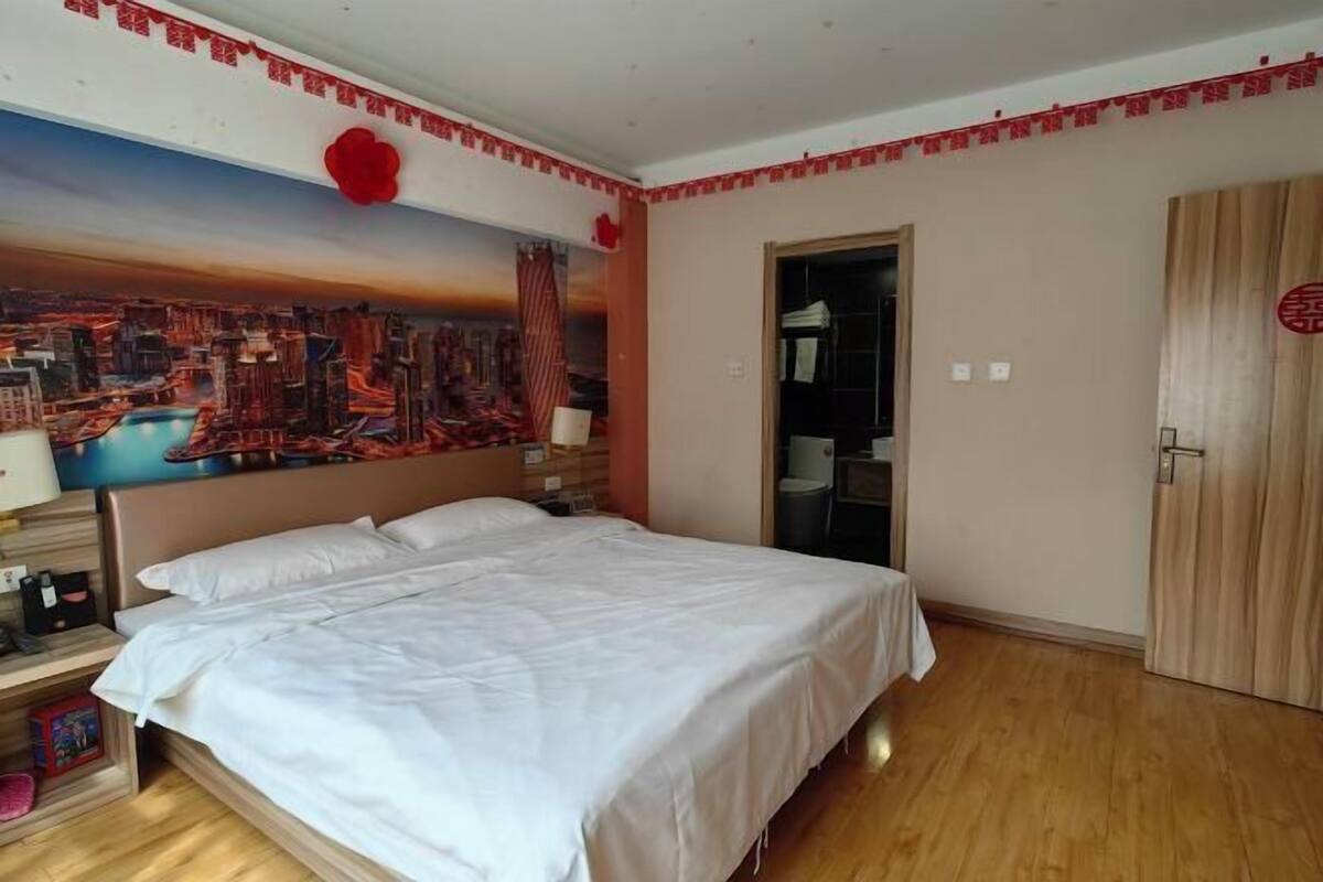 Een hotelkamer met een bed, nachtkastje, muurschildering, kledingkast en een deur met een rood symbool.