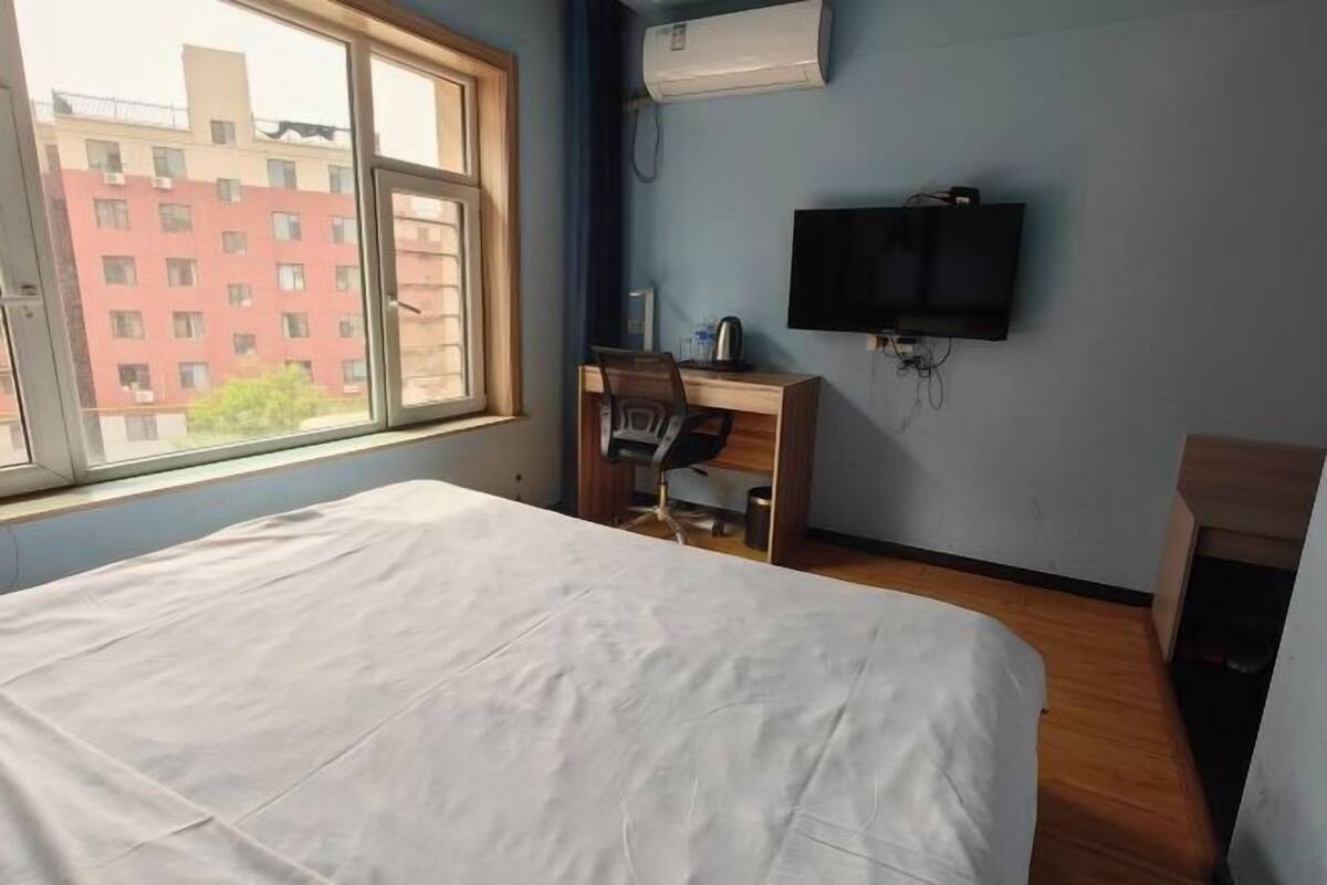 Een slaapkamer met een bed, een bureau met stoel, een televisie en een raam.