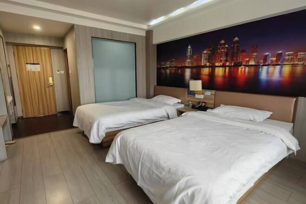 Een hotelkamer met twee bedden, een stadsgezicht schilderij aan de muur, en een houten deur.